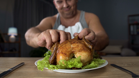 Bad-mannered overweight man tearing piece of chicken with hands, overeatingの写真素材