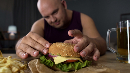 Obese man cooking big burger overeating gourmet admiring his meal close-upの写真素材