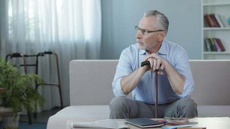 Retired male sitting on sofa at nursing home and thinking about life, sadnessの写真素材