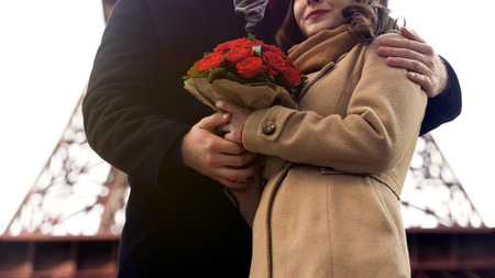 Man gently hugging beloved woman with nice flowers in hands, romance in Parisの写真素材