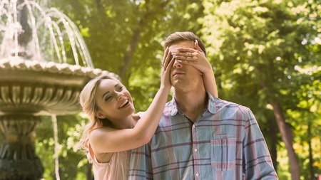 Girl closing eyes to her boyfriend, making surprise, loving couple on dateの写真素材