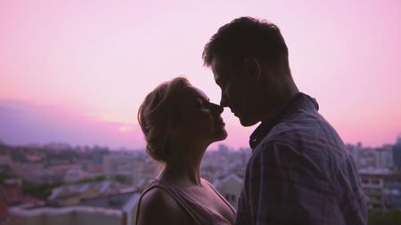 Cute lovers gently hugging, standing on roof, beautiful sunset city background, stock footageの写真素材