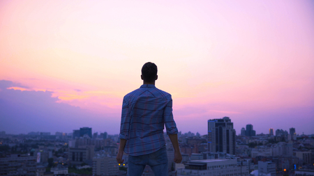 Free man standing on roof edge at dusk, desire to find strength and independenceの写真素材