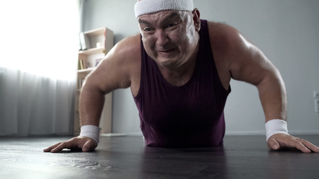 Motivated plump man in his 50s doing push-up with great effort, home trainingの写真素材
