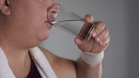 Close-up of chubby man drinking fresh water from glass, healthy weight loss dietの写真素材
