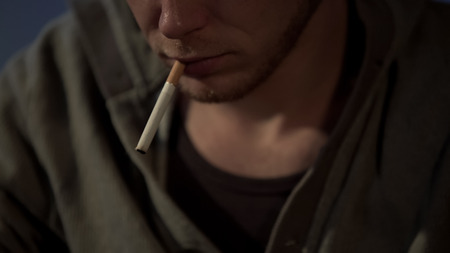Young man smokes cigarette, depressed and abandoned, health risks, close up, stock footageの写真素材