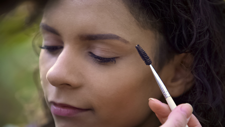 Makeup artist preparing beautiful young woman for shoot, enhancing eyebrowsの写真素材
