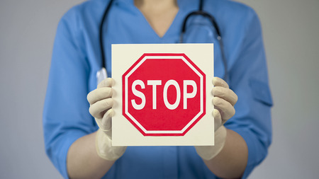 Doctor holding stop sign, warning about unhealthy lifestyle, harmful habitsの写真素材