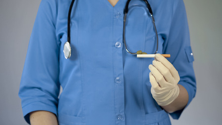 Female doctor holding cigarette in hand, cancer warning, bad habit addiction