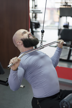 Strained young man working out in the gym, sports exercises for healthy life