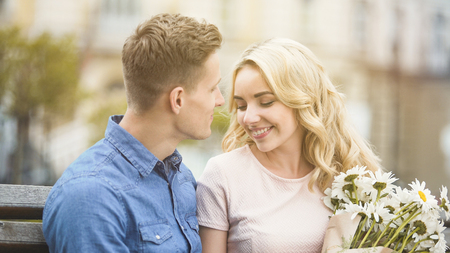 Beautiful blonde girl smiling to beloved man, holding nice bunch of flowersの写真素材