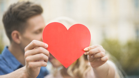 Boyfriend and girlfriend cuddling and hiding behind paper heart, romantic loveの写真素材