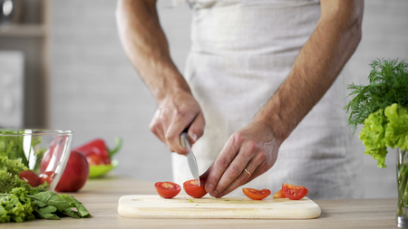 Male chef cutting tomatoes on table for fresh vegetable salad home, weight lossの写真素材