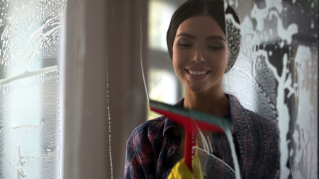 Young happy woman wiping glass surface after spray, cleaning service qualityの写真素材