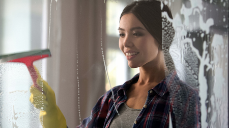 Wife wiping glass door of her apartment from dust and stains, house-proud woman