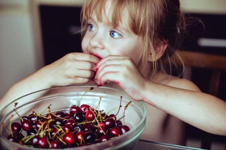 Portrait of a little smiling girl sitting with a face smeared in cherriesの写真素材