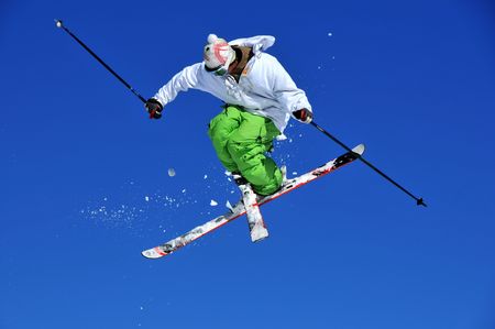 skier in green and white clothes performing a tele-heli with skis crossed at the same time as executing a full spin (in this shot, facing backwards)の写真素材
