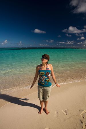 Young woman standing on tropical white sand beach by turquoise watersの写真素材