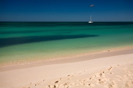 Boat on turquoise waters seen from the white sand beach of a tropical islandの写真素材