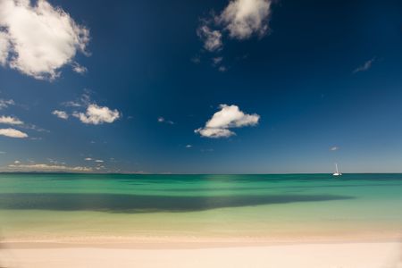 Boat on turquoise waters seen from the white sand beach of a tropical islandの写真素材
