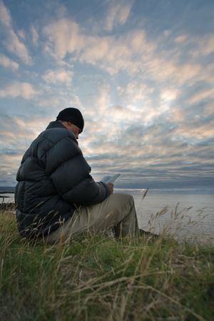 Young man reads a book by the ocean under dramatic skies, Faroe Islands, Scandinaviaの写真素材