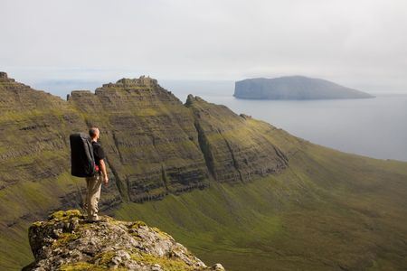 Young man backpacking among green mountains high above the ocean, Faroe Islands, Scandinaviaの写真素材