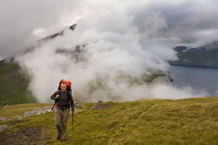 Young man walking among misty green mountains high above the ocean, Faroe Islands, ScandinaviaFaroe Islands, Scandinaviaの写真素材