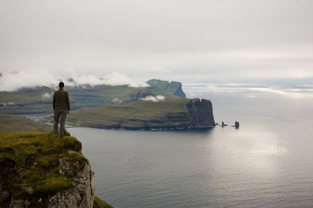 Young man stands at the edge of a cliff abve the ocean, Faroe Islands, Scandinaviaの写真素材