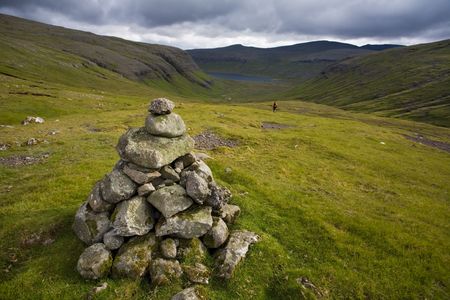 Hiker makes his way down a green valley, with cairn in the foreground, Faroe Islands, Scandinaviaの写真素材