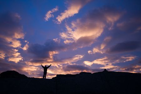 Silhouette of person with raised arms against dramatic sunset sky, Norway, Scandinaviaの写真素材