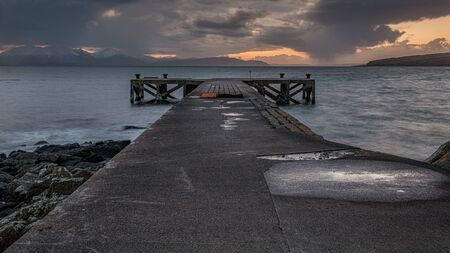 The old jetty at Portencross in Scotland and winter hills on the isle of Arran just as the sun goes down producing a dramatic sunset sky.の写真素材