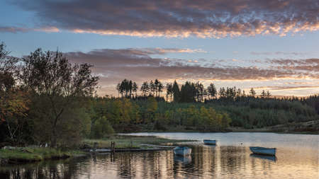 Fishing boats on Loch Rusky at sunrise, a small freshwater loch near Callander in the Scottish Highlands.の写真素材