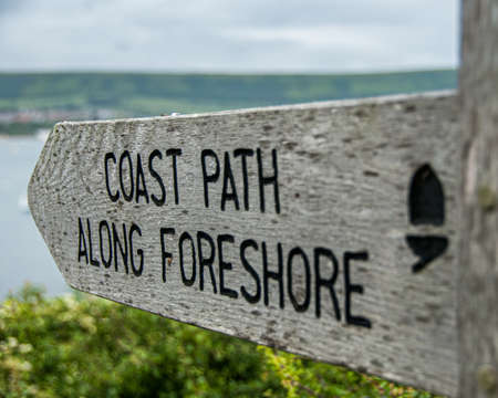 A weathered wooden sign post indicating the route of a coastal path along the foreshore in Southern Englandの写真素材