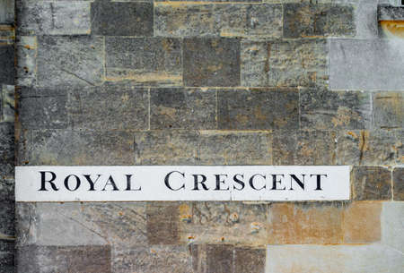 A street sign for Royal Crescent in Bath painted onto the corner of an old textured stone wall outside the housesの写真素材