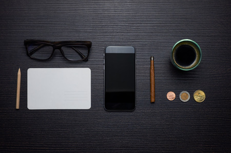 Smart phone, cigarillo, coins, coffee, glasses and card on the wooden tableの写真素材