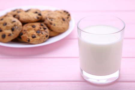 Glass of milk and chocolate cookies on plate on pink wooden backgroundの写真素材