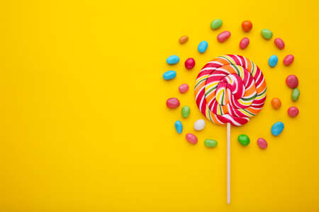 Colorful lollipops and different colored round candy on yellow