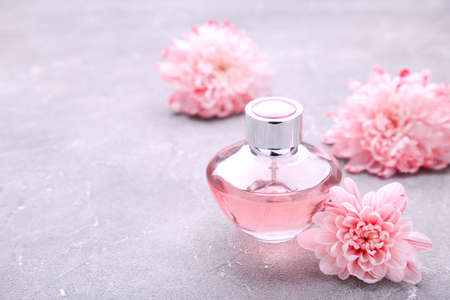 Bottle of perfume with flowers on gray background with copy space