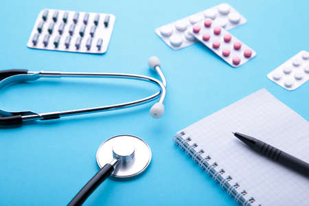 Stethoscope with notebook and pills on blue background. Top viewの写真素材