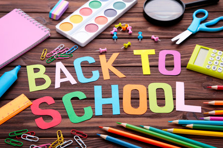 Inscription Back To School with school supplies on brown background. Education