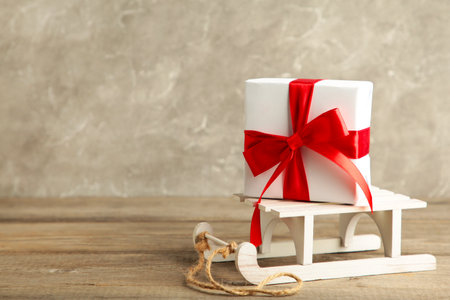 White sleigh with gift on gray wooden background. Christmas composition