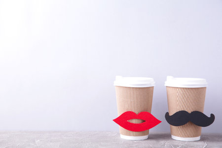 Paper cup of coffee with lips and mustache decoration on gray background, top view. Valentine's day and wedding concept.の写真素材