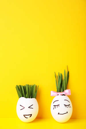 Funny handmade eggs with hair of green grass with copy space. Easter concept on yellow backgrund,...