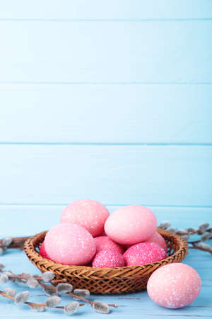 Colorful easter eggs in basket and willow branches on blue. Easter concept