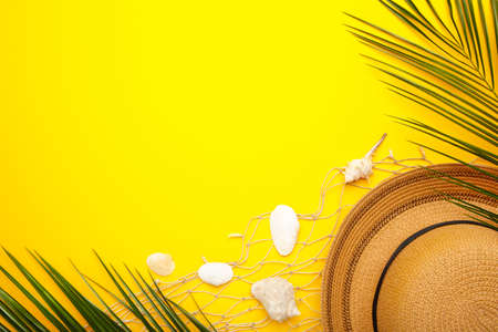 Beach hat with seashells and palm leaves on yellow background. Top view