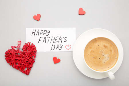 Fathers Day message with coffee cup and hearts on gray background. Top view
