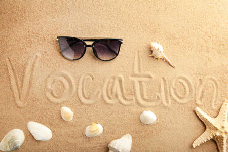 The inscription Vocation and beach accessories on the sandy beach. Top view