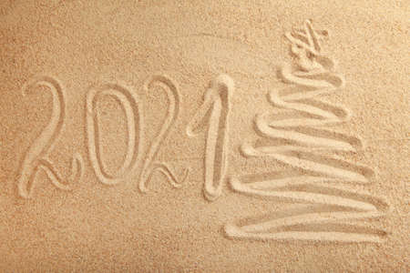 2021 new year text with christmas tree on sand background. Top view