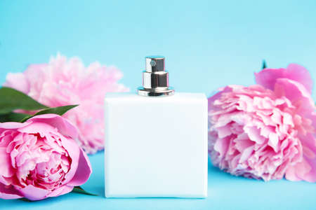 White bottle of perfume with pink flowers on blue background with copy spaceの写真素材