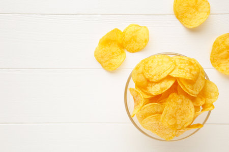 Potato chips on bowl on white wooden background. Top view